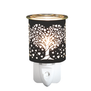 A black plug-in electric wax melt warmer with a tree and heart cutout design emits a warm glow. The elegant design creates a serene, delicate atmosphere.