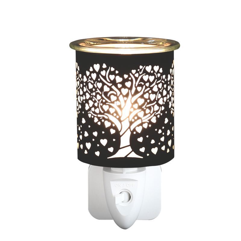 A black plug-in electric wax melt warmer with a tree and heart cutout design emits a warm glow. The elegant design creates a serene, delicate atmosphere.