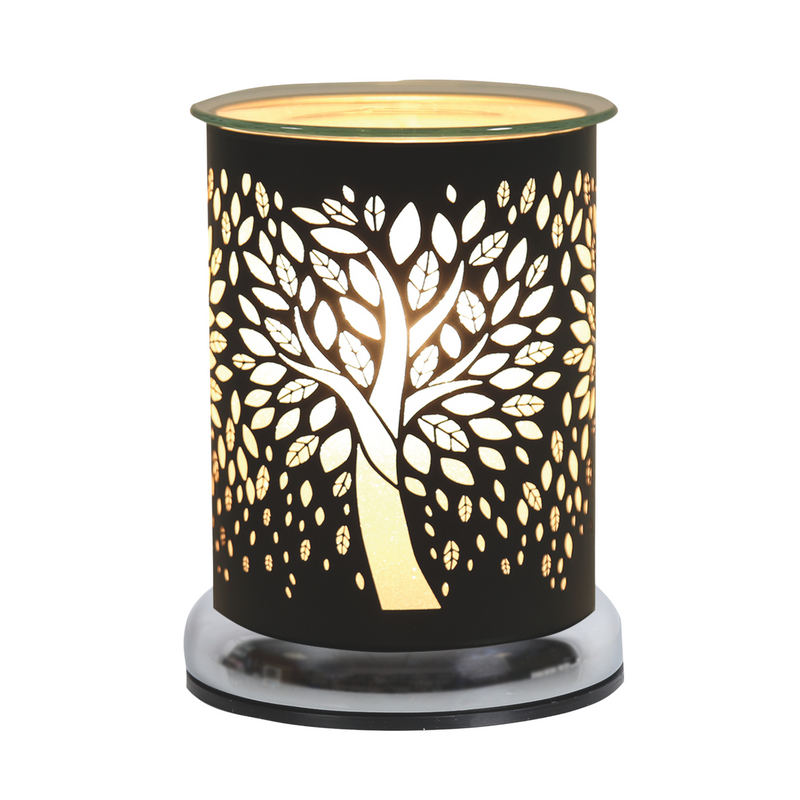 A black cylindrical electric wax melt warmer, adorned with a tree cutout design, glowing warmly. The metal surface contrasts with the soft light, creating a cosy ambiance.