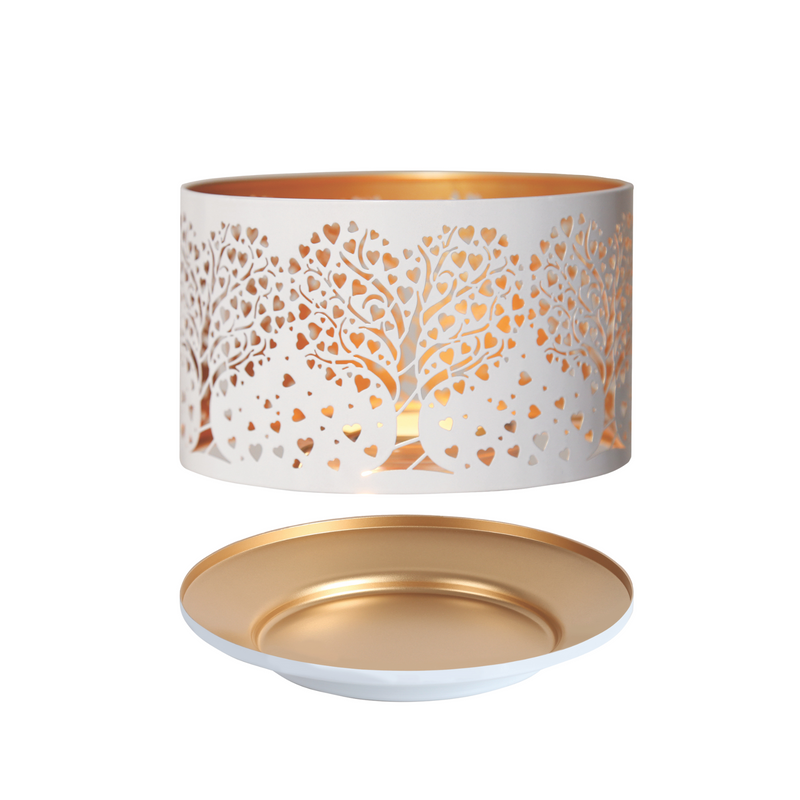 A white, cylindrical candle shade with heart-shaped tree cutouts, glowing warmly from within. It sits above a matching gold and white candle tray.
