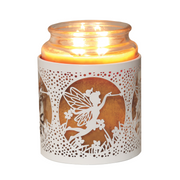 A lit candle in a glass jar, encased in a decorative white metal holder featuring a fairy silhouette design with flowers. The scene is warm and whimsical.