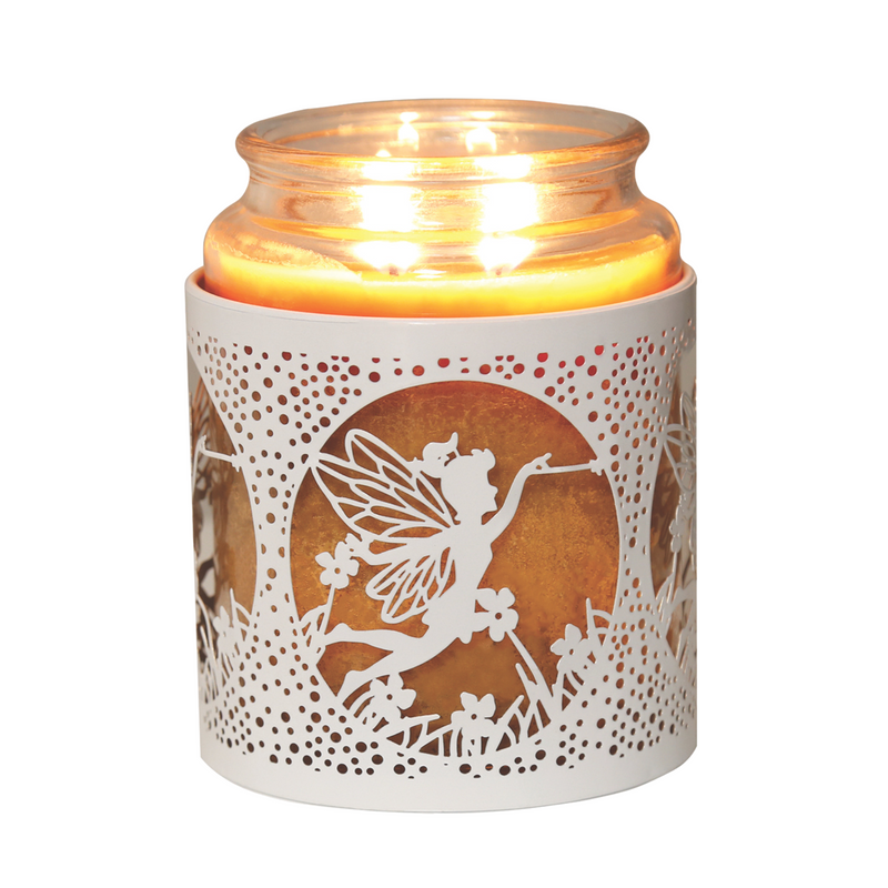 A lit candle in a glass jar, encased in a decorative white metal holder featuring a fairy silhouette design with flowers. The scene is warm and whimsical.