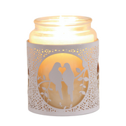 Lit candle in a glass jar with a decorative white sleeve featuring two doves perched on a branch, creating a warm, romantic ambiance.