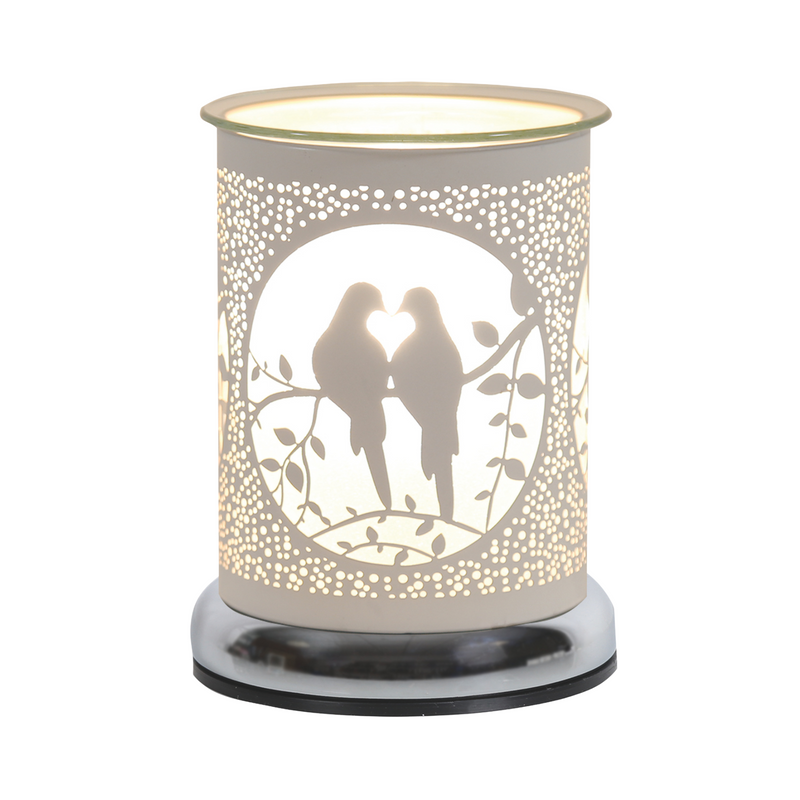 A decorative white electric wax melt warmer features two silhouetted birds on a branch, enclosed in a circular frame. Warm light glows, creating a cosy, romantic ambiance.