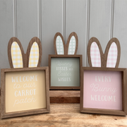 Three wooden signs with bunny ears, featuring pastel colors and Easter-themed messages: "Welcome to our carrot patch," "Bunny kisses and Easter wishes," and "Every bunny welcome."