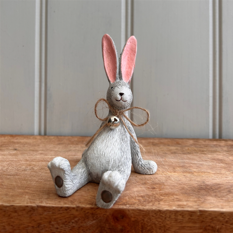 A whimsical Laidback Sitting Bunny Rabbit Ornament figurine, Grey with pink ears and a twine bow sits playfully on a wooden surface, conveying a cheerful and rustic vibe.