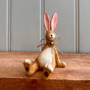 A whimsical Laidback Sitting Bunny Rabbit Ornament figurine, Bunny Brown with pink ears and a twine bow sits playfully on a wooden surface, conveying a cheerful and rustic vibe.