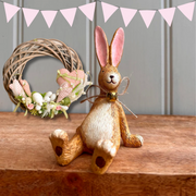 A whimsical Laidback Sitting Bunny Rabbit Ornament figurine, Bunny Brown with pink ears and a twine bow sits playfully on a wooden surface, conveying a cheerful and rustic vibe.