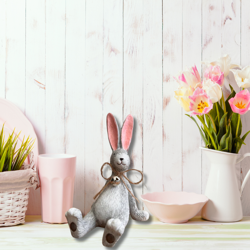 A whimsical Laidback Sitting Bunny Rabbit Ornament figurine, Grey with pink ears and a twine bow sits playfully on a wooden surface, conveying a cheerful and rustic vibe.
