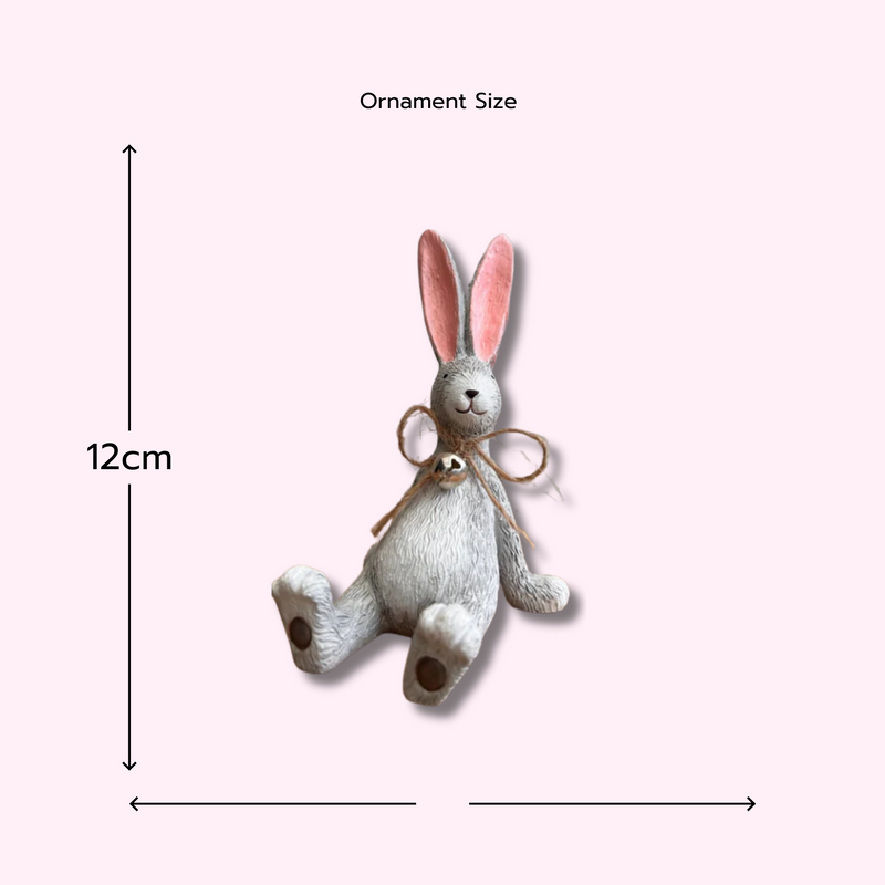 A whimsical Laidback Sitting Bunny Rabbit Ornament figurine, Grey with pink ears and a twine bow sits playfully on a wooden surface, conveying a cheerful and rustic vibe.