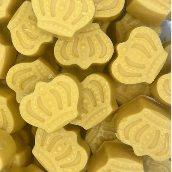 Yellow crown-shaped wax melts are closely packed together, with embossed details highlighting their royal design. The tone is playful and indulgent.