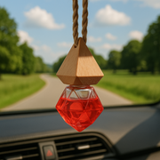 Car Fragrance Diffuser Air freshener with a wooden cap and red bottle hangs from a car's rearview mirror. It overlooks a sunny countryside road lined with lush green trees.