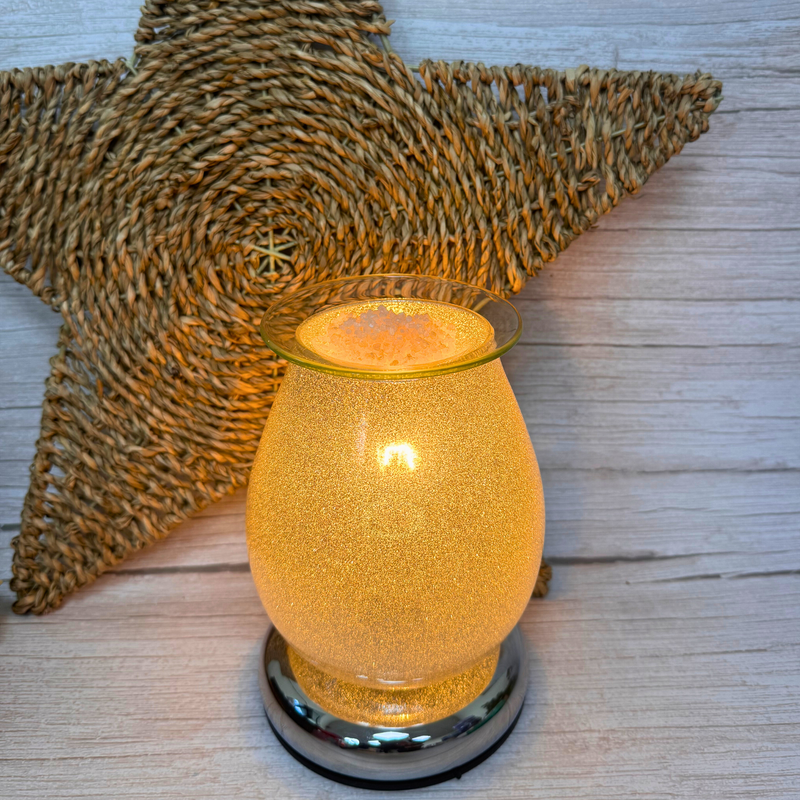 Glowing electric wax melt warmer on a wooden surface with a woven star backdrop. Warm ambiance with a metallic base, conveying cozy and rustic vibes.