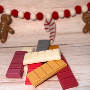 Colorful wax melt snap bars on a wooden surface with Christmas decorations in the background.