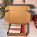 Open cardboard box containing wax melt snap bars on a wooden surface with Christmas decorations.