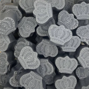 Close-up of numerous gray, crown-shaped soaps stacked haphazardly. Each wax melt features detailed embossed patterns, conveying a playful and elegant tone.