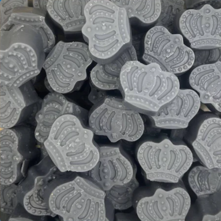 Close-up of numerous gray, crown-shaped soaps stacked haphazardly. Each wax melt features detailed embossed patterns, conveying a playful and elegant tone.