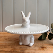 White ceramic cake stand featuring a rabbit motif, with a rabbit head on top and body as the base. The design is clean and whimsical, perfect Spring cake stand.