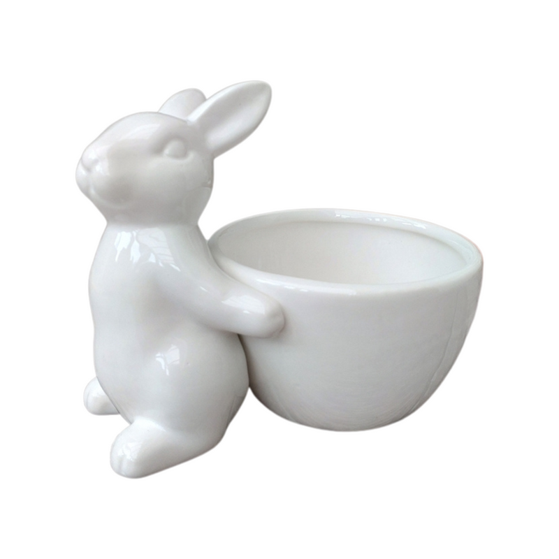 White ceramic bunny rabbit with an attached bowl. The bunny is sitting upright, holding the bowl, conveying a whimsical tone.