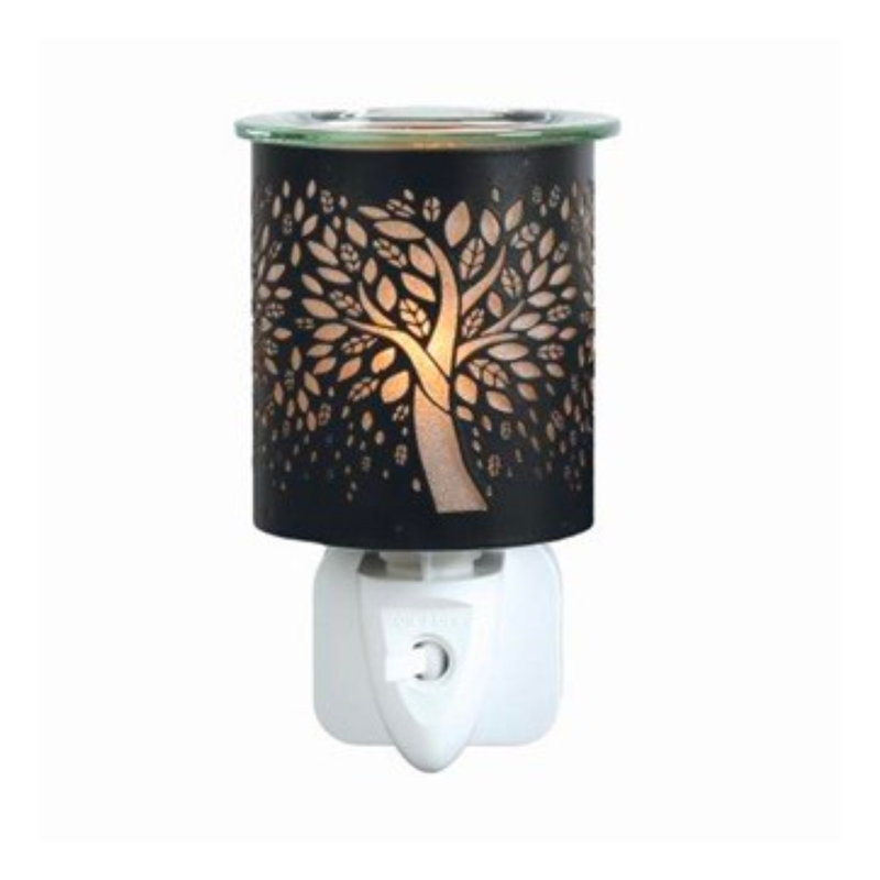 A black & gold plug-in wax melt warmer with a cut-out tree design glows warmly. The intricate branches and leaves create a calming, ambient effect.